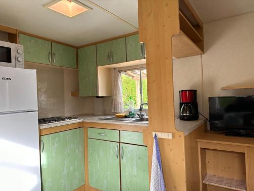 a kitchen with green cabinets and a white refrigerator at Mobil-home à quelques mètres du lac d'Aiguebelette in Novalaise