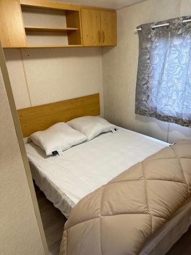 une petite chambre avec un lit avec des draps blancs et des oreillers dans l'établissement Mobil-home à quelques mètres du lac d'Aiguebelette, à Novalaise