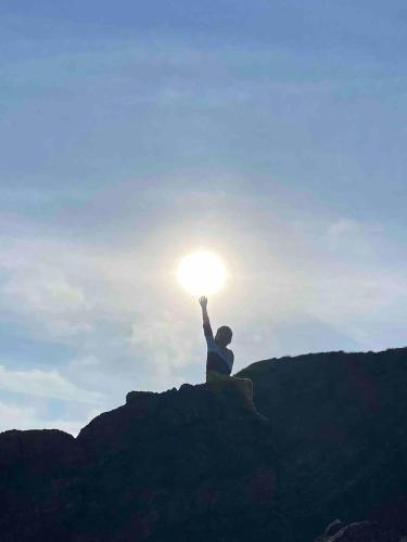 a person sitting on a rock holding up the sun at Ardmores Contemporary Beach House in Sluggera Cross Roads