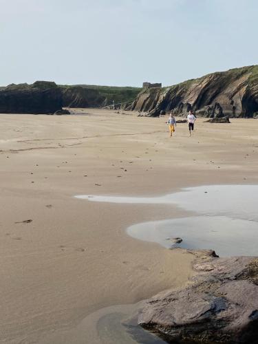 two people walking on the beach near the water at Ardmores Contemporary Beach House in Sluggera Cross Roads