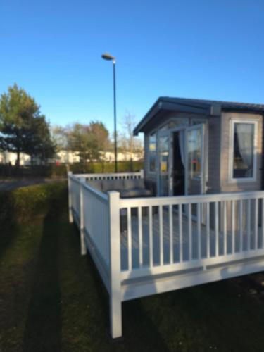 a small house with a white porch and a fence at Silver 3 Bed Static Caravan With Patio in Port Seton
