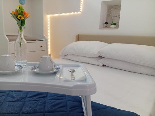ein weißes Bett mit einem Tisch mit einer Vase mit Blumen darauf in der Unterkunft CV MiRa house in Putignano