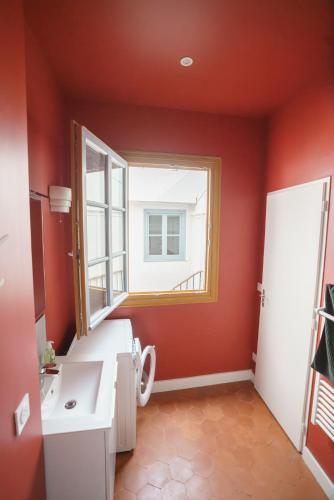 La salle de bains est pourvue de murs rouges, d'un lavabo et d'une fenêtre. dans l'établissement Le nid de la rue Mailly, à Perpignan