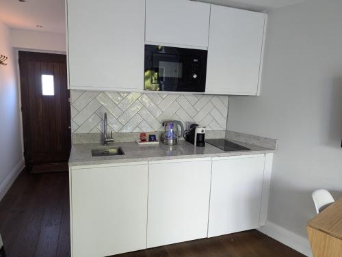 a kitchen with white cabinets and a sink at Ox Lane Annexe - Harpenden in Harpenden