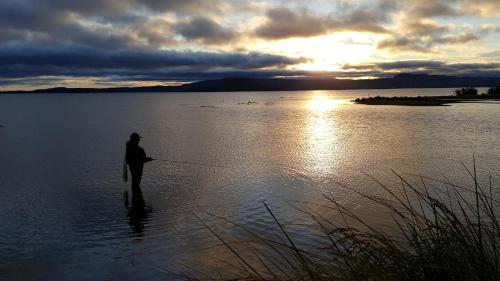 a man standing in the water holding a fishing rod at Lakeview Small Studio in Rotorua
