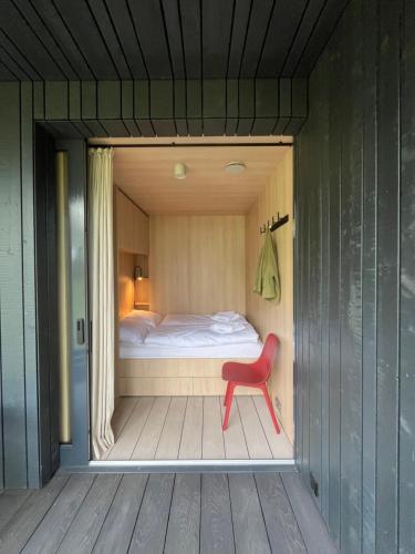 a room with a bed and a red chair at Capsula aan de Wadi in Diepenheim