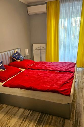 a bedroom with a bed with red sheets and yellow curtains at Koczor Apartman in Balatonfüred