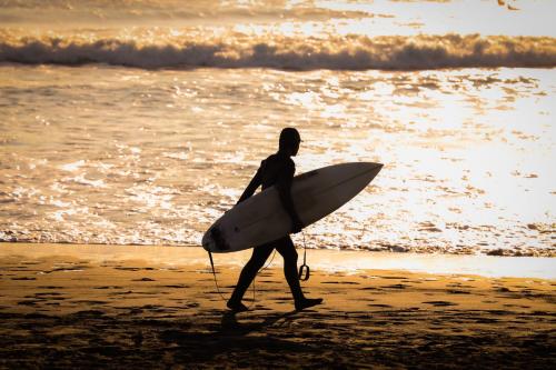 a man walking on the beach with a surfboard at Tabist Pension Third Place in Ichinomiya
