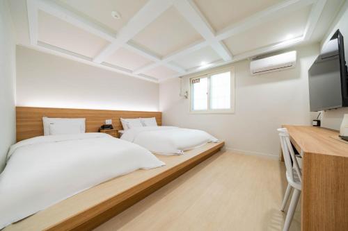 a bedroom with two beds and a desk and a tv at DongBaek Hotel Gohyeon in Geoje 