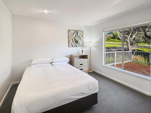 Un dormitorio con una cama grande y una ventana. en Oceanfront 4-Bed Haven with BBQ & Alfresco Dining, en Malua Bay
