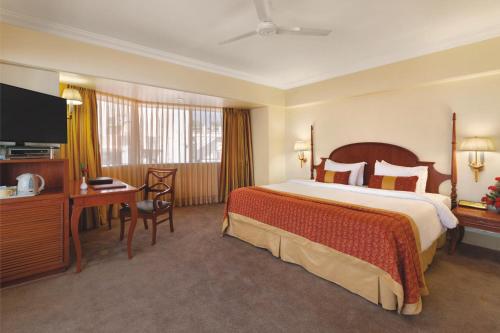 a hotel room with a bed and a desk and a television at Ramada Plaza By Wyndham Palm Grove in Mumbai