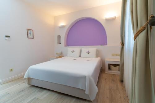 a white bedroom with a white bed and an arched window at Sigacik Gardenya Buti̇k Otel in Siğacık