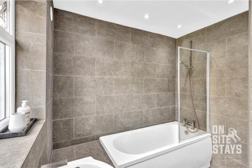 a bathroom with a white tub and a shower at OnSiteStays - Large 3 bedroom, 2 bathroom, driveway, Garden, Sleeps 6 Comfortably in Bexleyheath