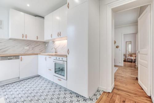 Il comprend une cuisine blanche avec des placards blancs et du parquet. dans l'établissement Delta - Appartement parisien - 9e, à Paris