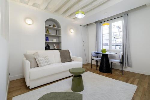 Huchette - Appartement chaleureux Paris في باريس: غرفة معيشة مع أريكة بيضاء وطاولة
