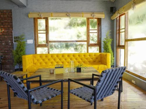 a yellow couch in a living room with a table and chairs at The Hosteller Mcleodganj, Upper Bhagsu in McLeod Ganj