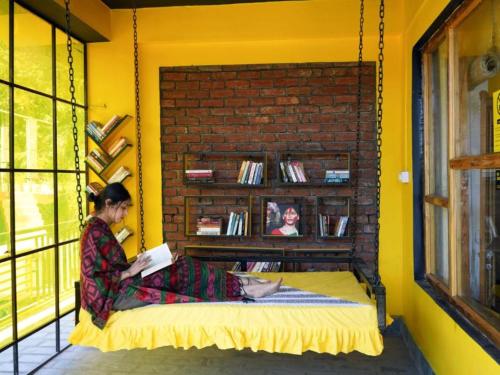 a woman sitting on a bed reading a book at The Hosteller Mcleodganj, Upper Bhagsu in McLeod Ganj