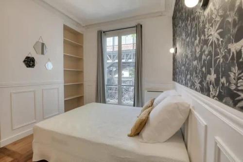 une chambre avec un lit blanc avec une grande fenêtre dans l'établissement Chapelle - Appartement familial au centre de Paris, à Paris