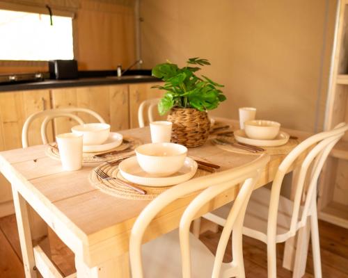 a wooden table with white dishes and a plant on it at Orla Ilha de Tavira Eco-Glamping in Tavira