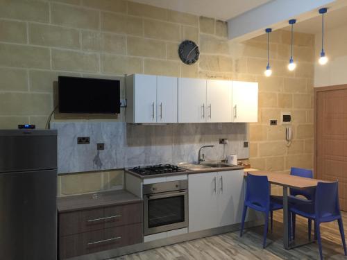 a kitchen with white cabinets and a table with blue chairs at Senglea Apartments in Senglea