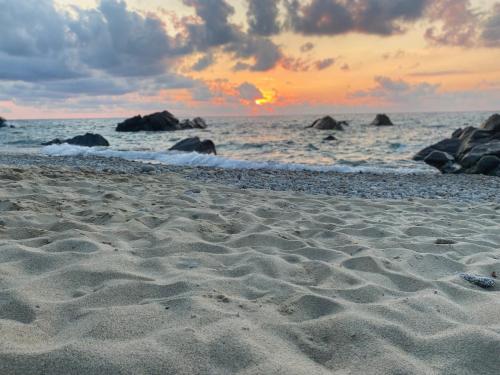 a sandy beach with rocks in the ocean at sunset at Villa Taurus Costa dei Monaci Parghelia Tropea in Parghelia