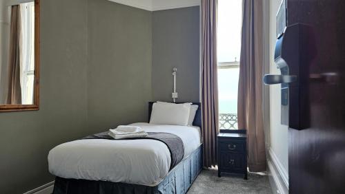 a small bed in a room with a window at The Strand Hotel in Eastbourne