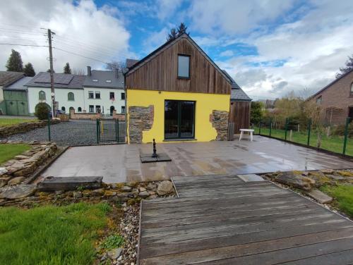 a yellow building with a wooden deck in front of it at La Catiche in Bastogne