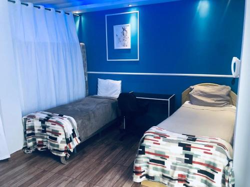 two beds in a room with blue walls at Flat do Bispo in Uberlândia
