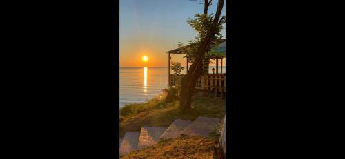 a sunset over the ocean with a house and a tree at Къща за гости Беглик таш 3 in Primorsko