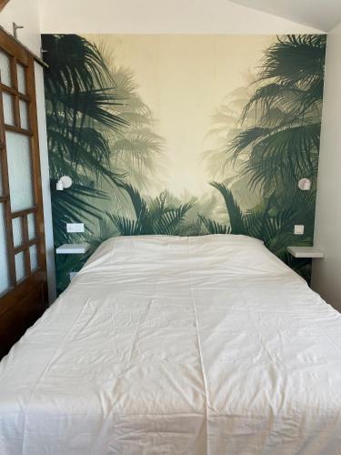 - une chambre avec un lit blanc et des palmiers sur le mur dans l'établissement Appartement cosy, à Béziers