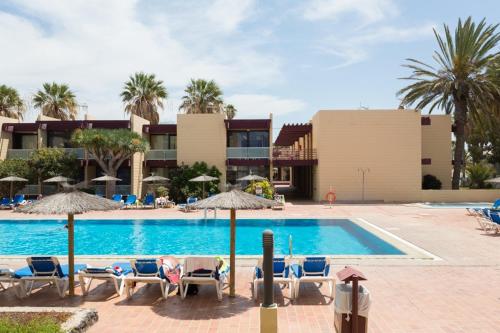 a swimming pool with chairs and umbrellas next to a building at Apartamento Hércules in Costa Del Silencio