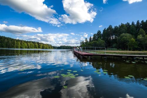a bridge over a lake with trees and clouds in the sky at Ośrodek Wypoczynkowy Kołatek in Olsztynek