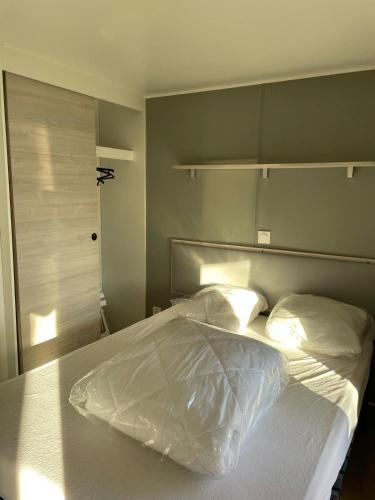 un lit avec des draps blancs et des oreillers dans une chambre dans l'établissement Mobil Home Lège Cap ferret bassin, à Lège-Cap-Ferret