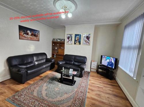 a living room with a black leather couch and a television at Spacious two bedroom house, parking and WiFi in Leeds