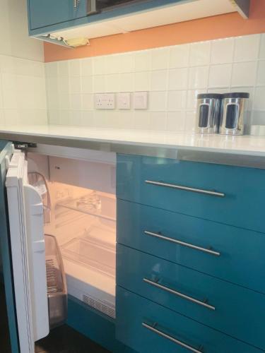 a kitchen with an open refrigerator and blue cabinets at The Apartment at Estuary Escapes in Kingsbridge