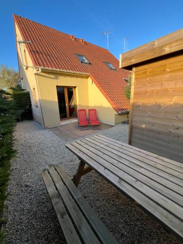 a bench in front of a building with two red chairs at Maison proche de la mer in Le Crotoy