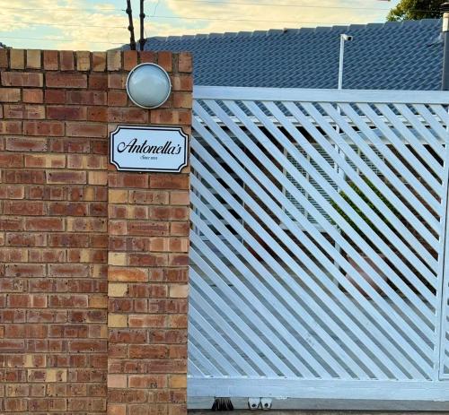 a sign on a brick wall next to a white fence at Antonella's in Edenvale