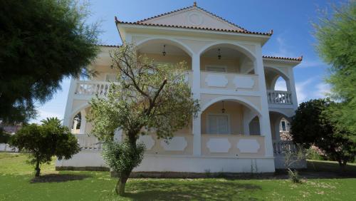 una grande casa bianca con un albero di fronte di Meltemi Standard Studios a Kalamákion