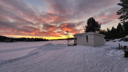 a small building in the snow with a sunset in the background at House with a spectacular view over Torne river in Kiruna