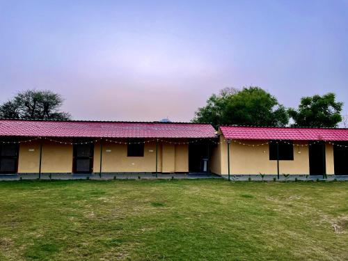 a building with red roofs with a field in front at The Vaas Woods - A Garden Homestay in Jaipur