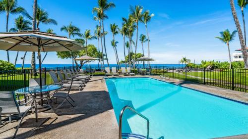 a swimming pool with chairs and umbrellas and the ocean at Kona Isle B22 in Kailua-Kona