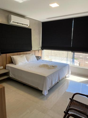 a bedroom with a white bed with a large window at Hotel Bonanzza Coxim in Coxim