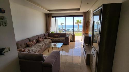 a living room with a couch and a table and a television at Appartement Plage des Nations Prestigia Front Mer avec grand Jardin in Sidi Bouqnadel
