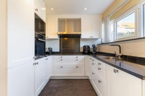 a white kitchen with white cabinets and a sink at Cosy house with 3 rooms and garden near beach in Ostend
