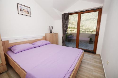 een slaapkamer met een bed met paarse lakens en een raam bij Apartmani Mizdrak in Kotor