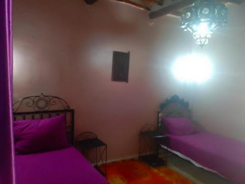 two beds in a room with purple sheets and a chandelier at Lamtounipalace in Ouarzazate