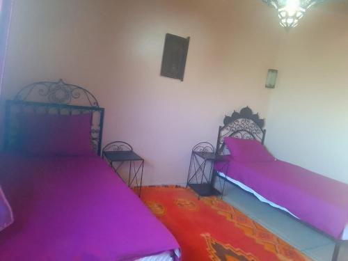 two beds in a room with pink sheets and two chairs at Lamtounipalace in Ouarzazate