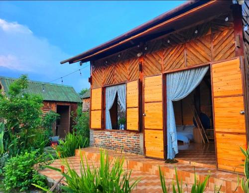 a wooden house with a porch in a garden at Nhà Bên Hồ 2- The Peace's House in Ấp Thánh Hương
