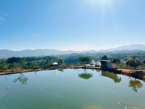 a large body of water with tents and mountains in the background at Giăng's House Farmstay & Glamping in Bao Loc