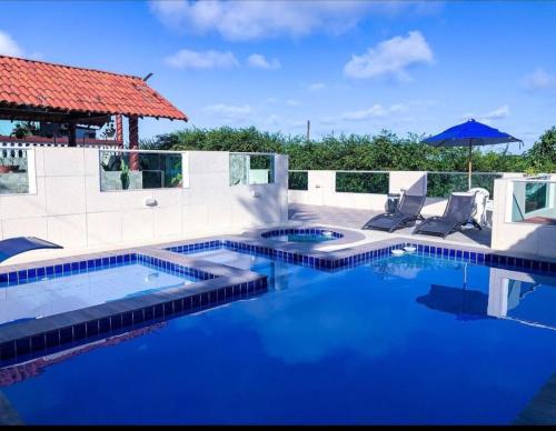 a swimming pool with blue water and two chairs and an umbrella at Villa Velha Flats in Itamaracá